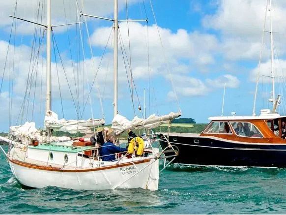 White sailing yacht alongside a dark motor yacht carrying passengers on the sea