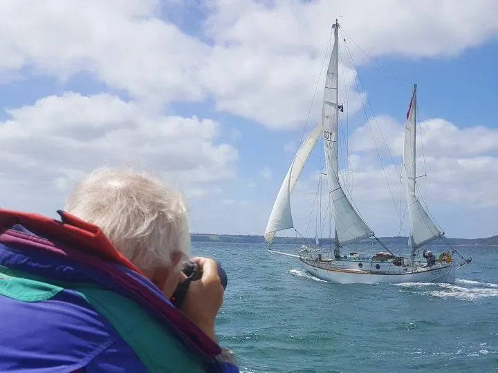 Person photographing a white two-masted sailing yacht on the sea