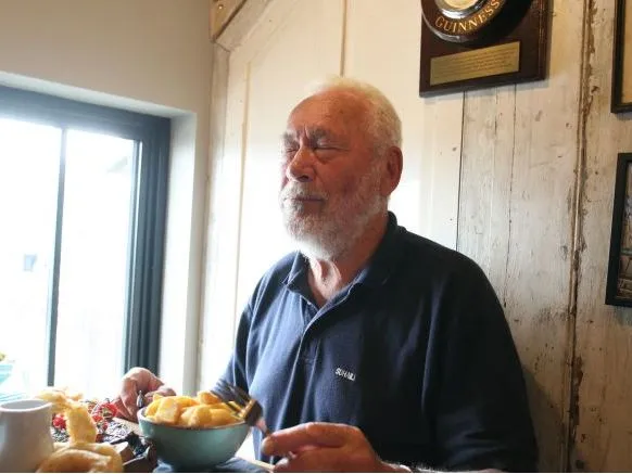 Older man with a white beard seated at a restaurant table with a bowl of food
