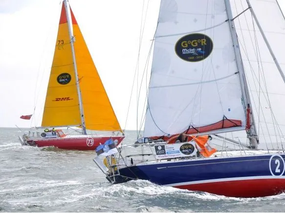Two racing yachts sailing across choppy water, one with white sails and a blue hull, the other with a bright orange sail.