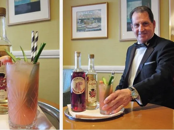 A pink cocktail with garnishes beside two bottles of spirits, shown alongside a smiling bartender in a tuxedo presenting the drink.
