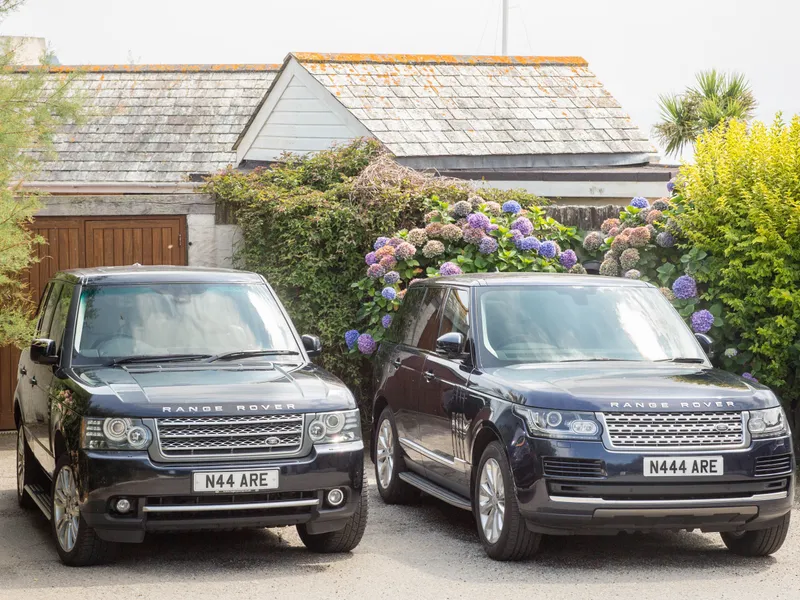 Two dark Range Rover SUVs parked side by side outside a cottage, with hydrangeas behind them
