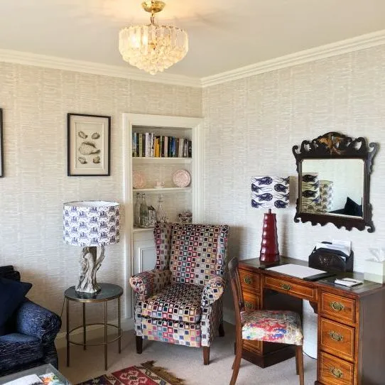 Elegant sitting room with a patterned armchair, navy sofa, wooden writing desk and crystal chandelier