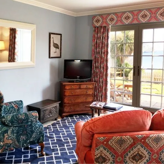 Colourful hotel sitting room with a patterned armchair, coral sofa and French doors opening towards the sea