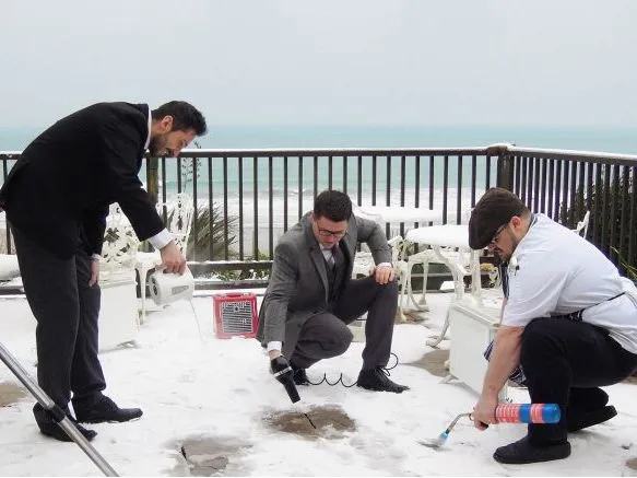 Four people clearing snow from an outdoor terrace overlooking the sea