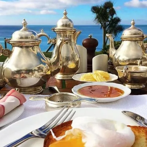 Breakfast table by the sea with silver teapots, poached eggs on toast, honey and butter