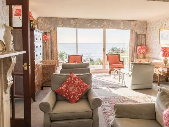 Elegant drawing room with upholstered armchairs, red patterned cushions and lamps, opening onto a sea view