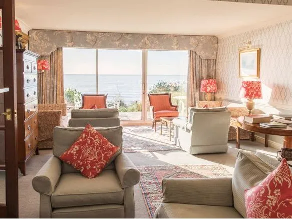 Elegant drawing room with upholstered armchairs, red patterned cushions and lamps, opening onto a sea view