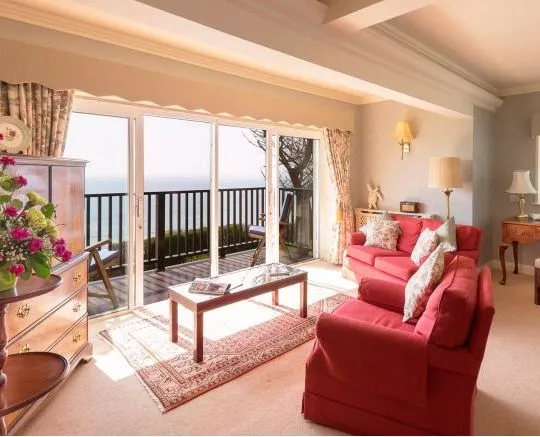 Sunlit sitting room with red sofas, antique wooden furniture and sliding doors opening onto a sea-view balcony