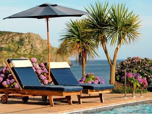Two navy sun loungers beneath a parasol beside a swimming pool overlooking the sea
