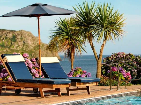 Two navy sun loungers beneath a parasol beside a swimming pool overlooking the sea