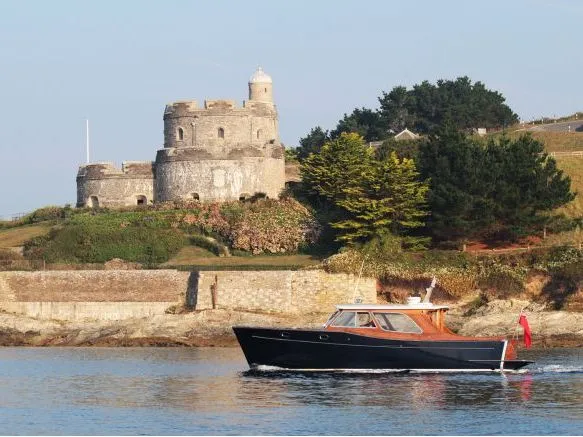 Dark-hulled motorboat cruising past a stone coastal fort on a grassy headland