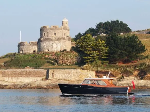 Dark-hulled motorboat cruising past a stone coastal fort on a grassy headland