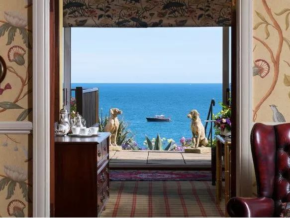 View through an elegant reception room doorway towards the blue sea, with a boat offshore and two dog statues on the terrace.