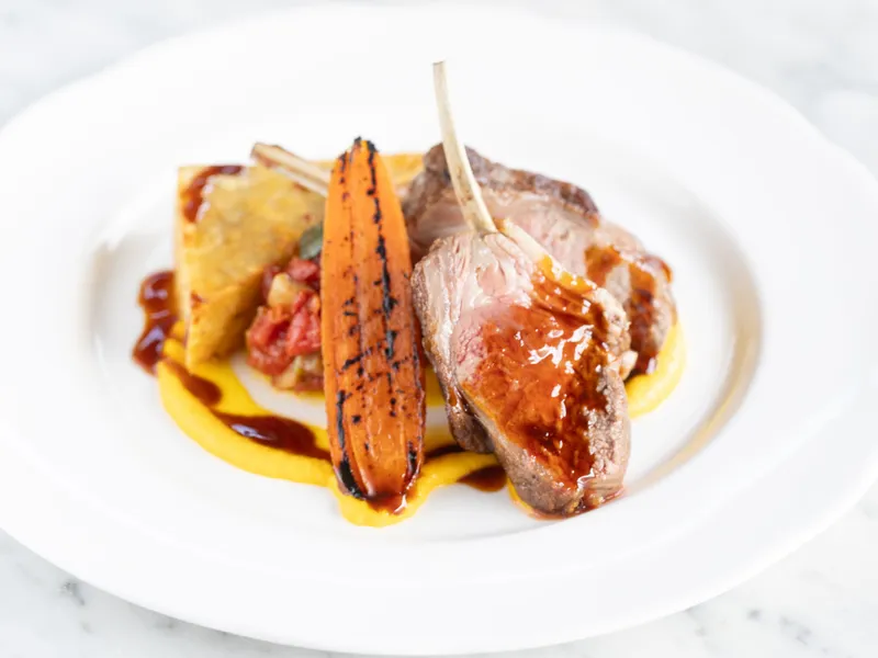 Plated lamb cutlets with glazed sauce, charred carrot and a golden side on a white plate.