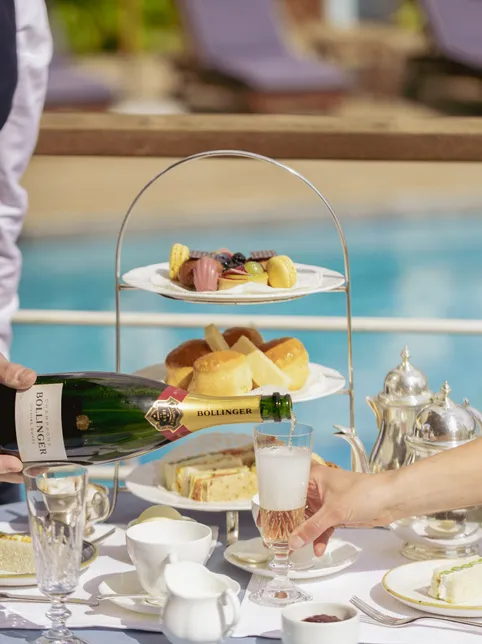 Waiter pouring champagne at an elegant afternoon tea table beside a swimming pool