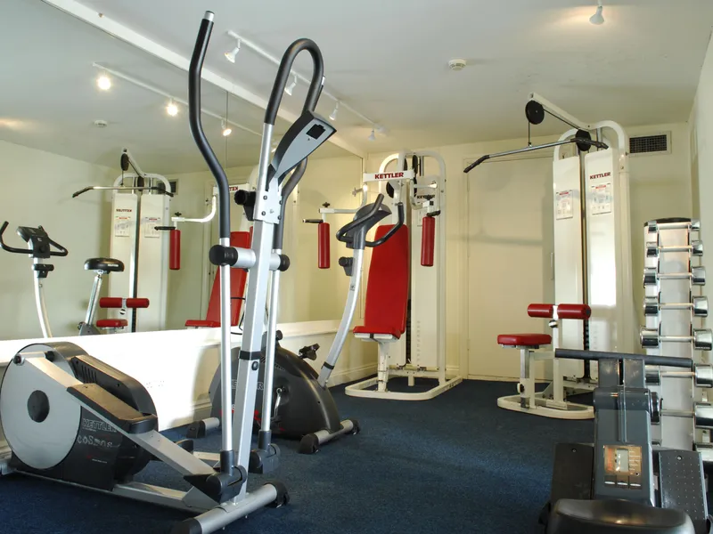 Compact indoor gym with cardio and weight machines, mirrored wall and free weights