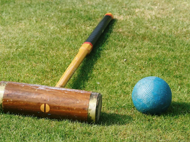 Wooden croquet mallet and blue ball on a neatly cut lawn