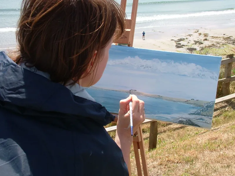 Art student painting a coastal landscape on an easel overlooking the beach