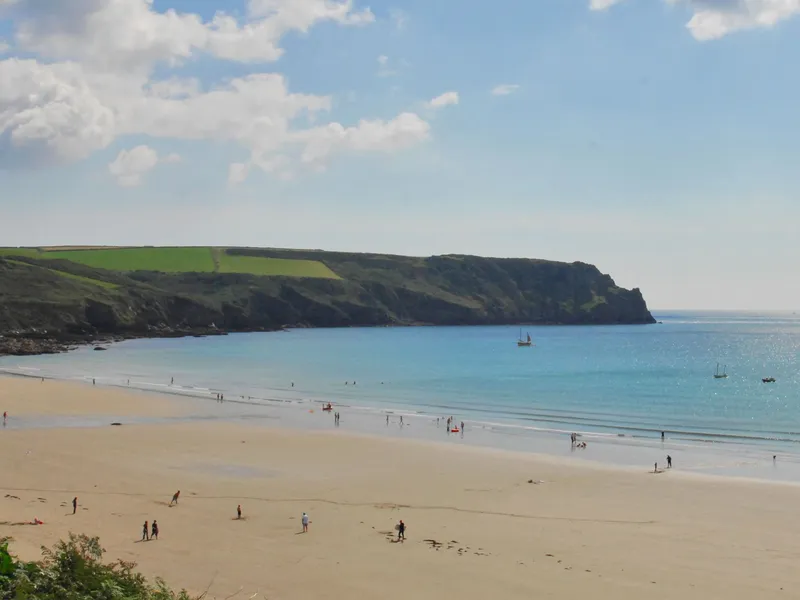 Wide view of The Nare beach with golden sand, calm turquoise sea, scattered people and boats beneath a bright blue sky.