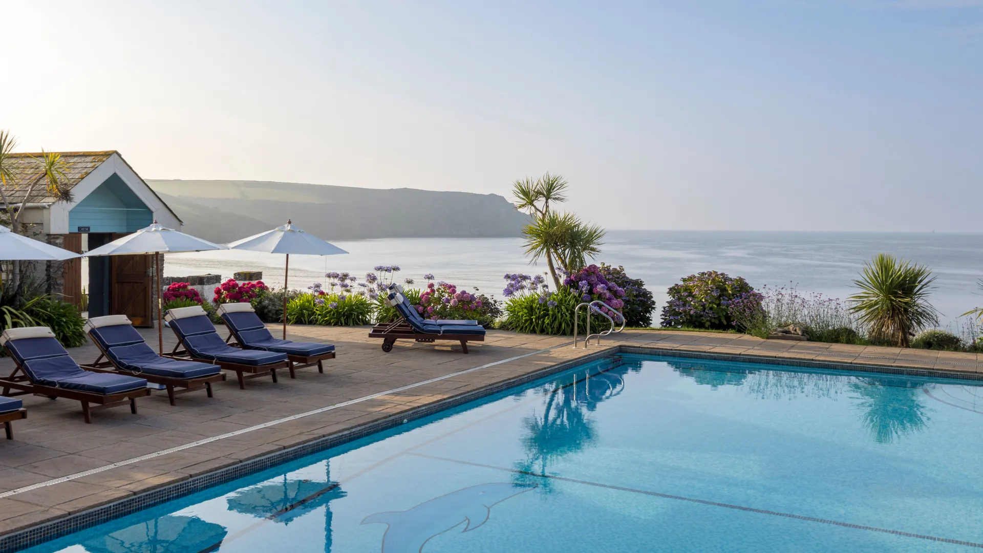 Outdoor swimming pool with sun loungers and parasols overlooking a calm coastal bay