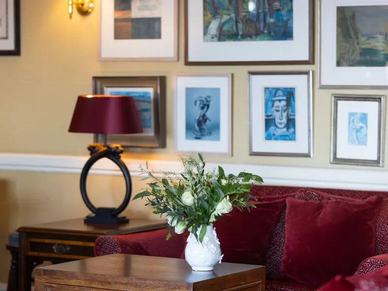 Cosy sitting area with red upholstered armchairs, wooden tables, framed artwork and warm lamp lighting