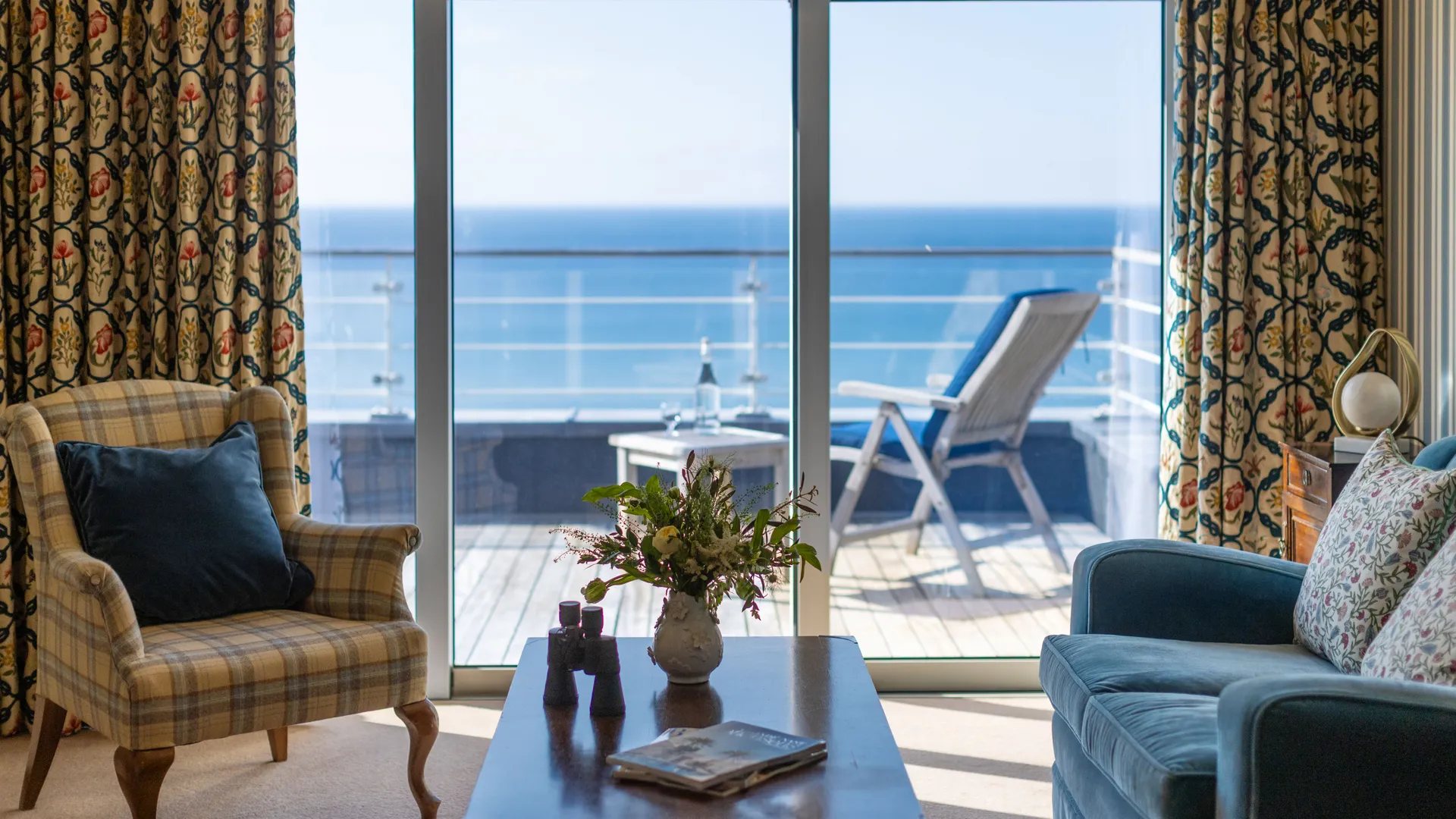 Elegant sitting room with patterned curtains, armchairs and a coffee table overlooking a private balcony and sea view.