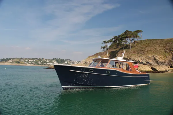 Dark blue motor boat anchored on calm coastal water near a rocky headland with pine trees