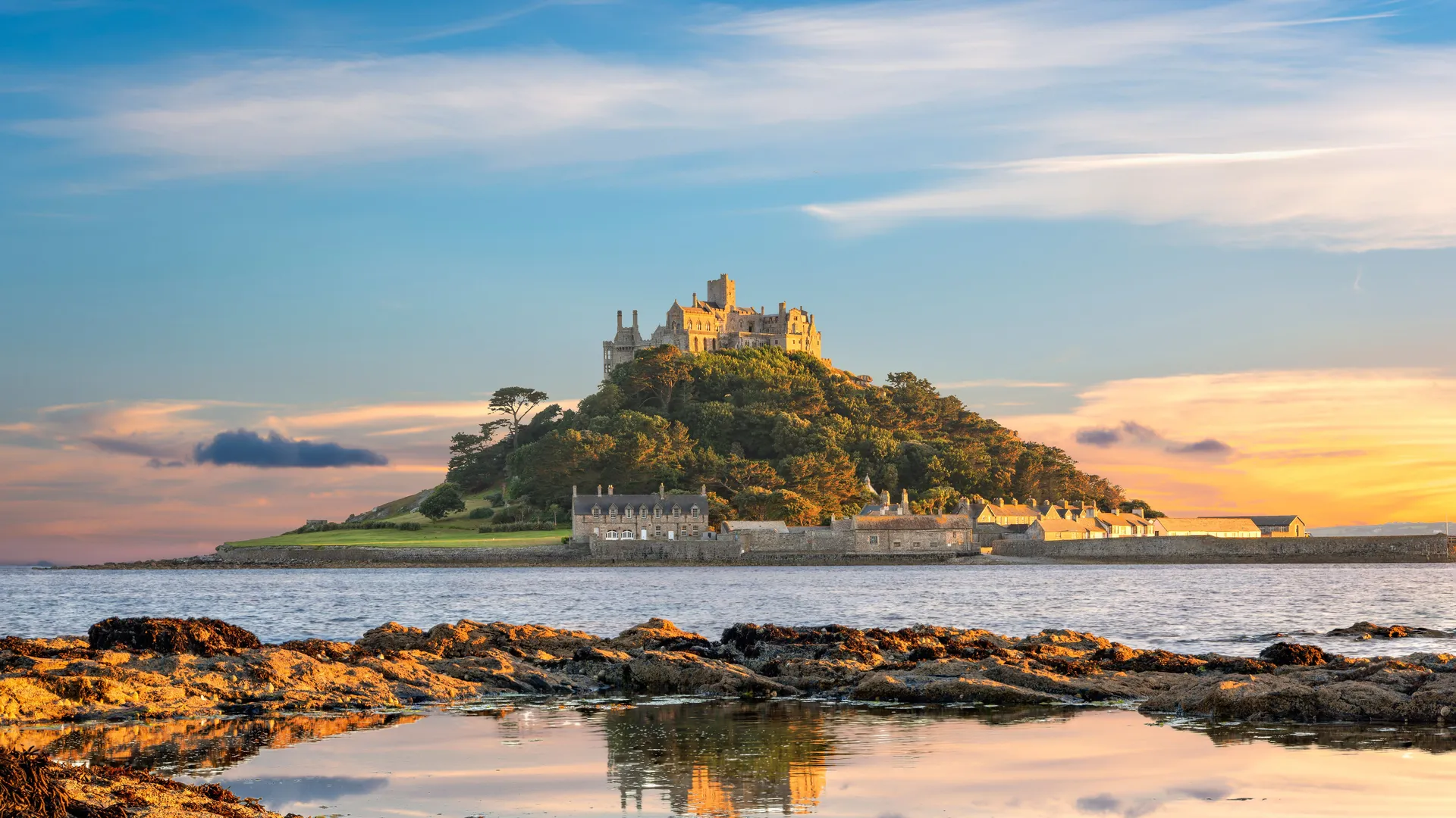 St Michael's Mount at sunset, reflected in a calm tidal pool with rocky shoreline in the foreground