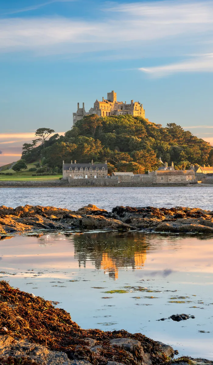 St Michael's Mount at sunset, reflected in a calm tidal pool with rocky shoreline in the foreground