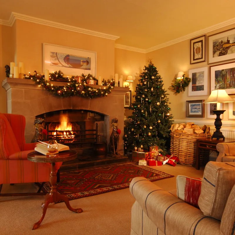 Cosy drawing room with a lit fireplace, decorated Christmas tree, festive garland and comfortable armchairs