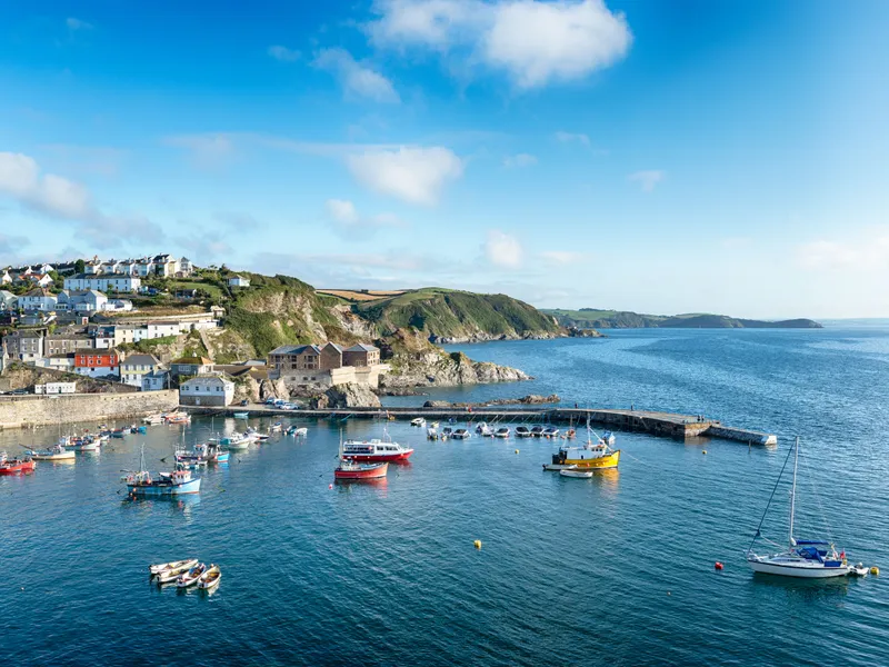 Mevagissey Coastal harbour village with colourful fishing boats, hillside houses and rocky cliffs under a bright blue sky