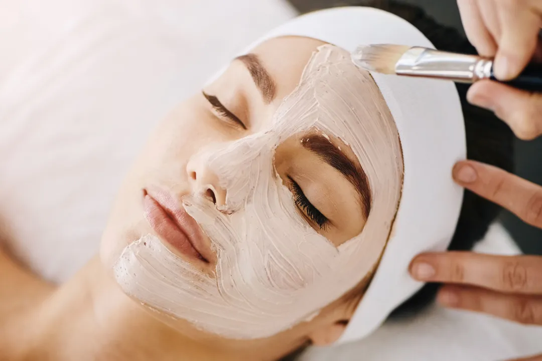 Woman relaxing with a facial mask being applied at a spa treatment