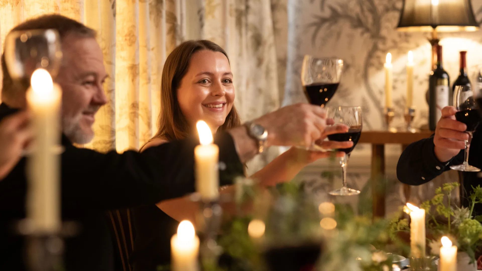 Friends toasting with glasses of red wine at a candlelit dinner table
