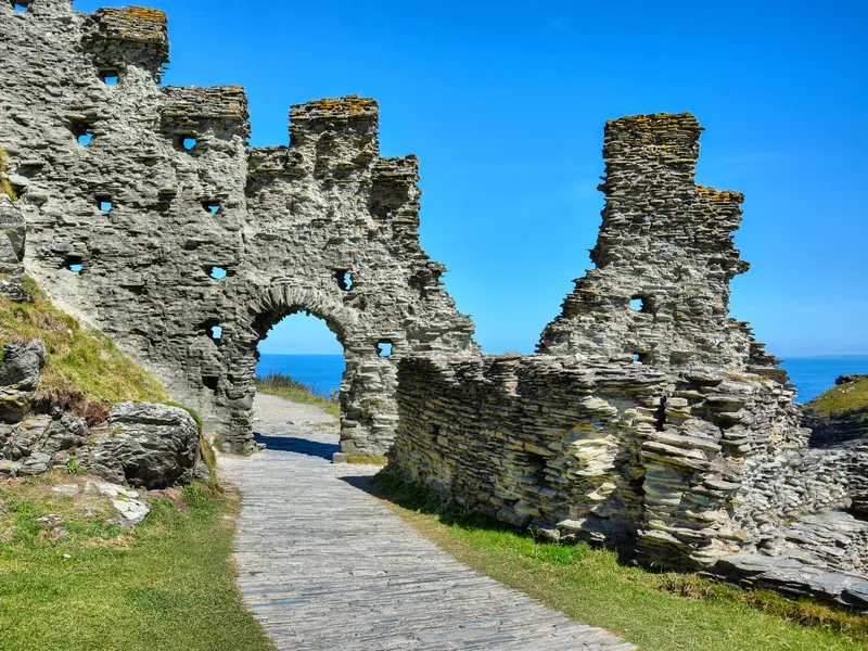 Ruined stone castle walls with an arched doorway on a coastal cliff under a bright blue sky