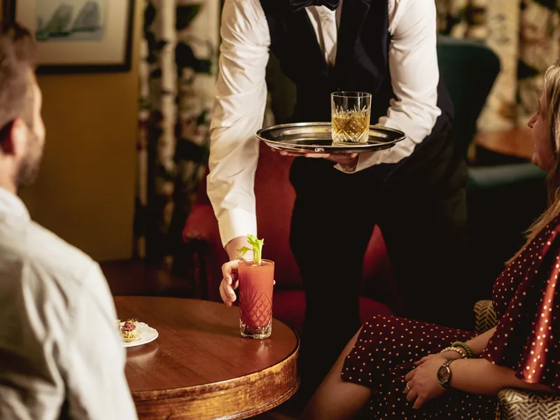 Waiter serving cocktails to a seated couple at a table in a warmly lit lounge