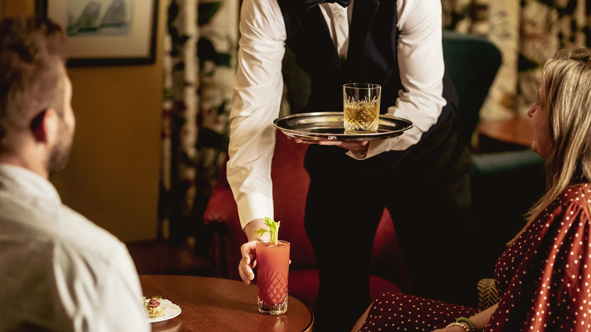 Waiter serving cocktails to a seated couple at a table in a warmly lit lounge