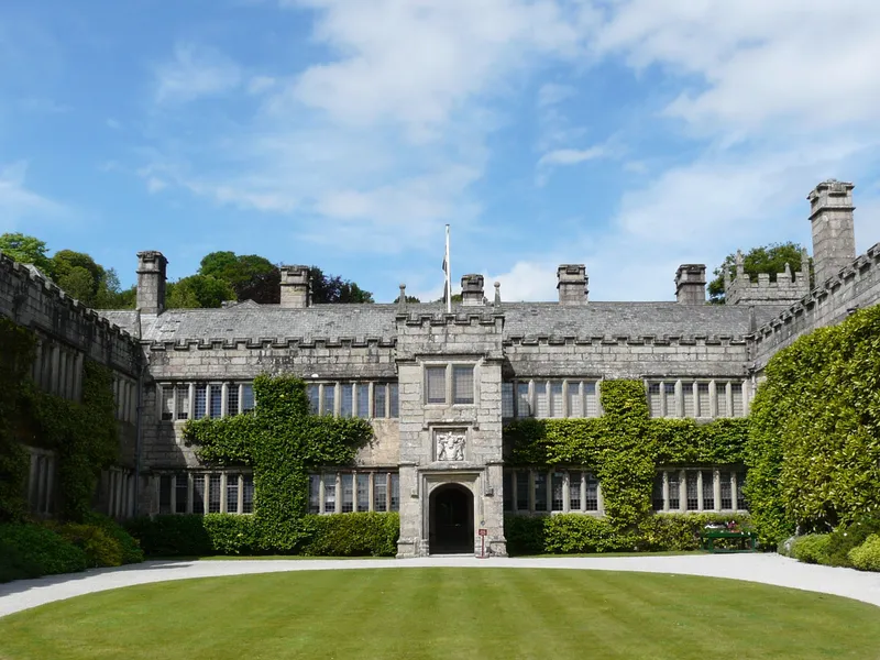Lanhydrock Castle Historic stone manor house with ivy-covered walls surrounding a circular lawn courtyard under a bright blue sky