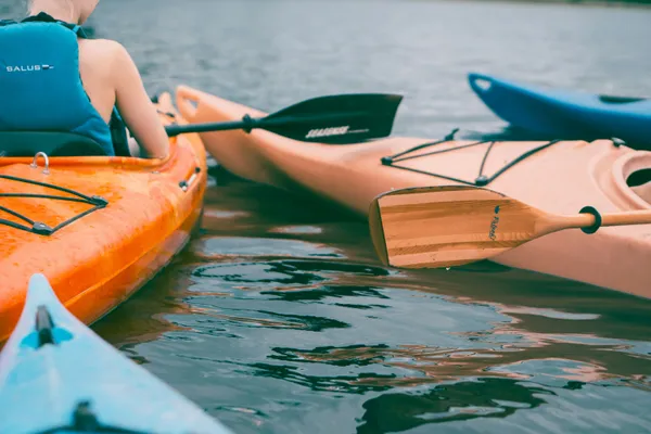 Person in a life jacket sitting in an orange kayak beside other kayaks on calm water