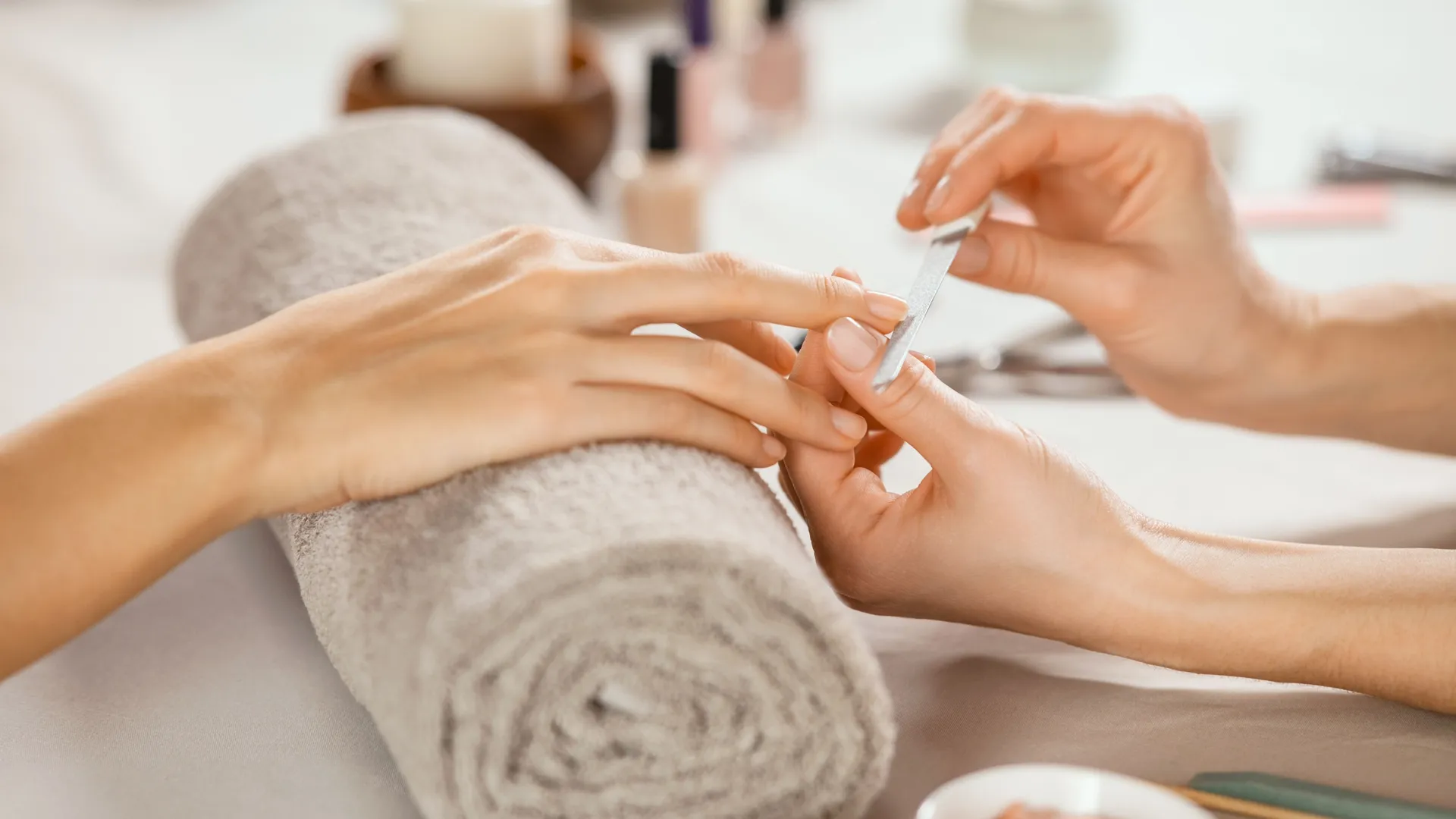Close-up of a manicure in progress, with a nail technician filing a client's fingernail over a rolled towel in a beauty salon.
