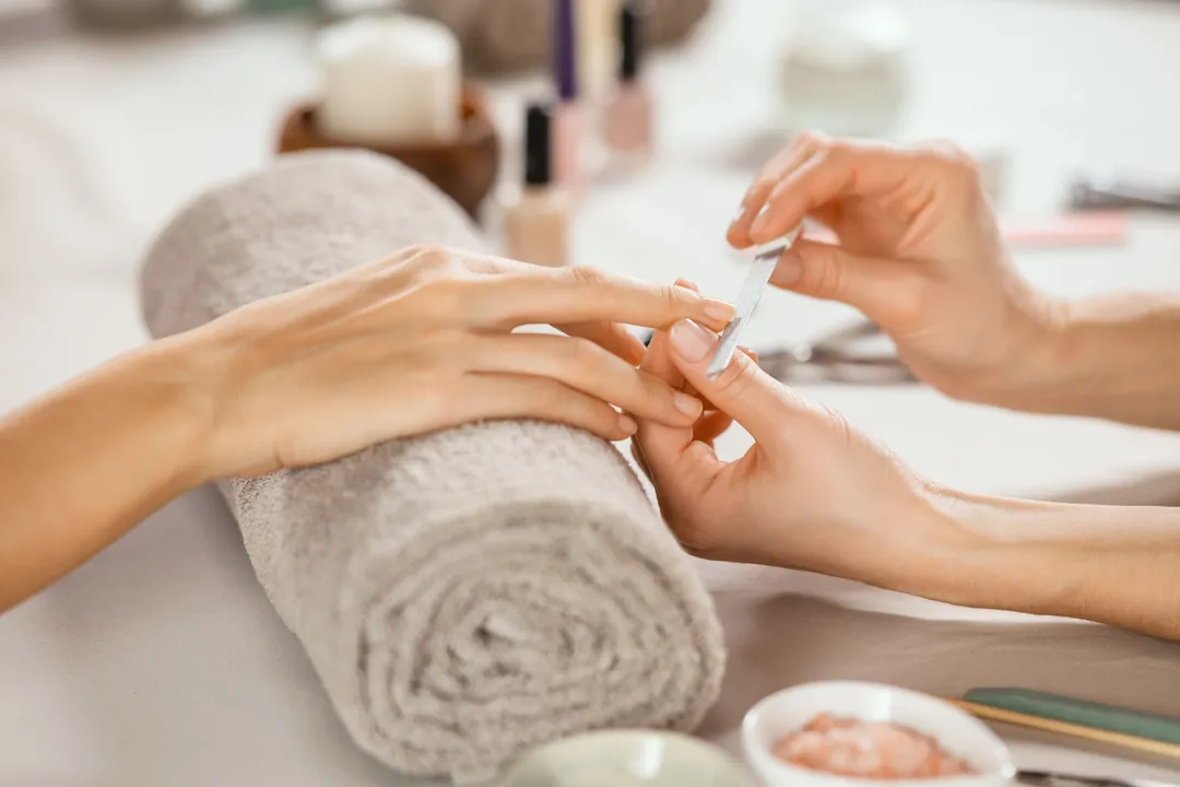 Close-up of a manicure in progress, with a nail technician filing a client's fingernail over a rolled towel in a beauty salon.