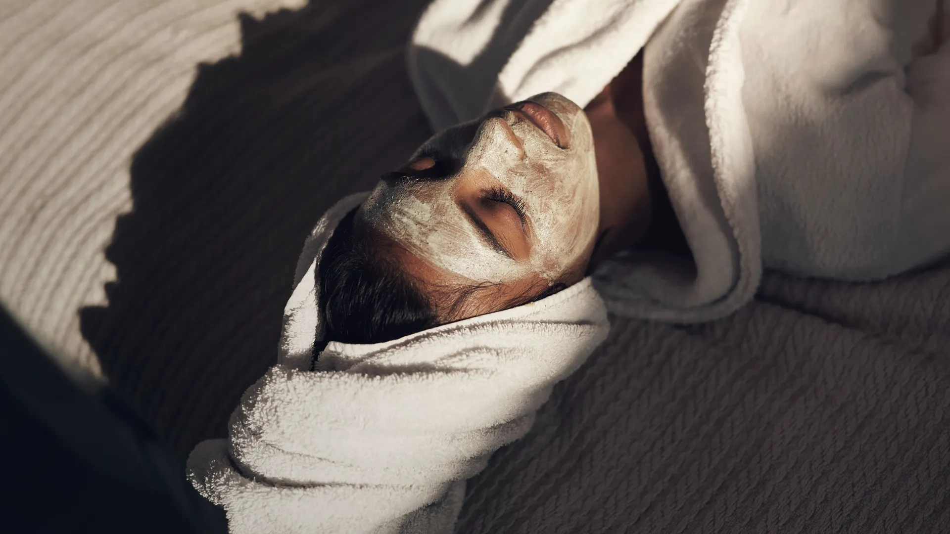 Woman relaxing with a facial mask and towel-wrapped hair in a spa setting