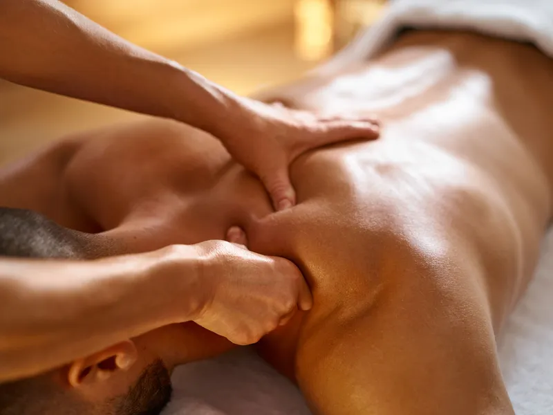 Therapist giving a deep tissue back massage to a man in a spa treatment room