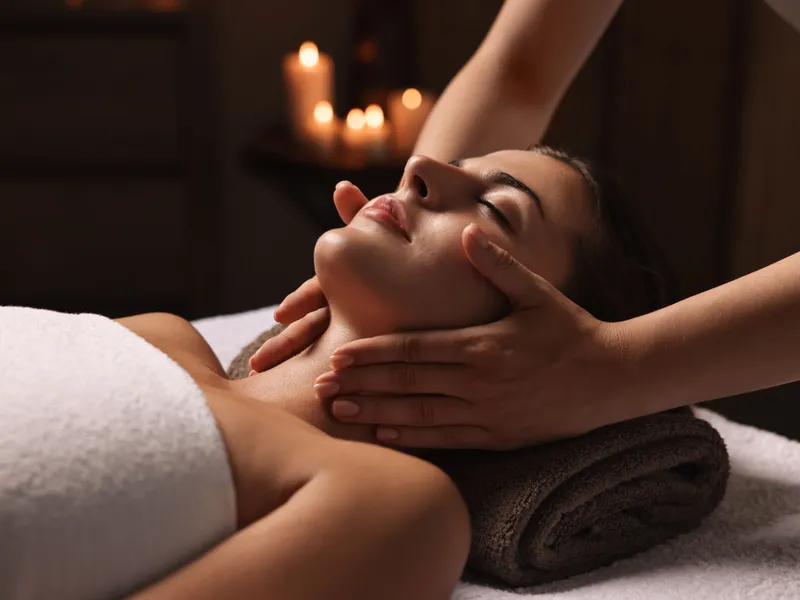 Woman receiving a relaxing neck and facial massage in a candlelit spa.