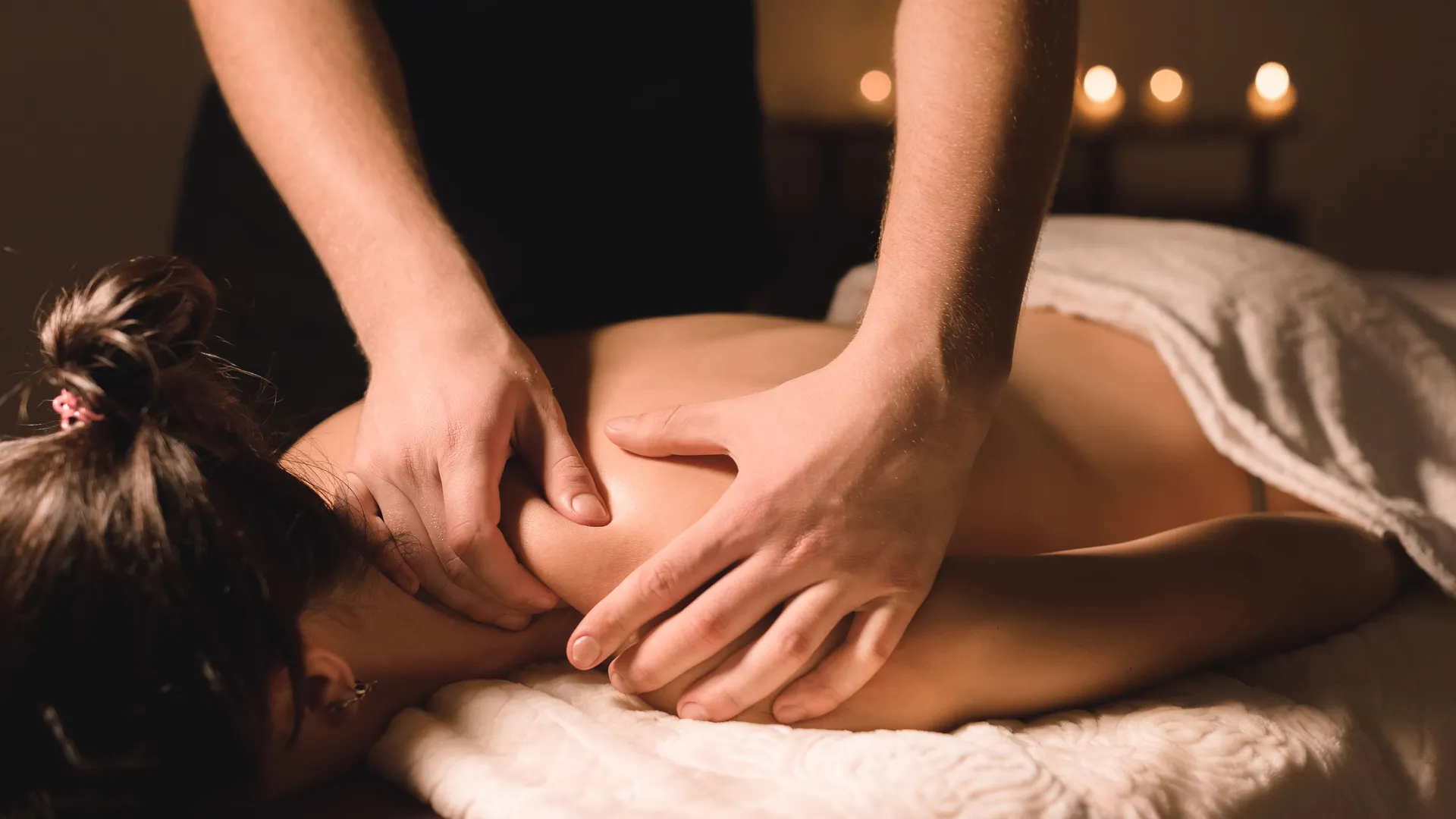 Person receiving a shoulder and upper back massage in a dimly lit spa with candles in the background