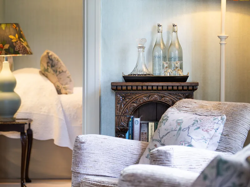 Cosy bedroom and sitting area with floral lampshades, framed bird artwork and an upholstered armchair
