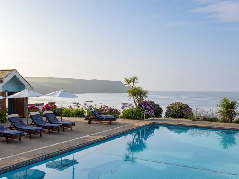 Outdoor swimming pool with sun loungers, parasols and sea views beside a coastal garden