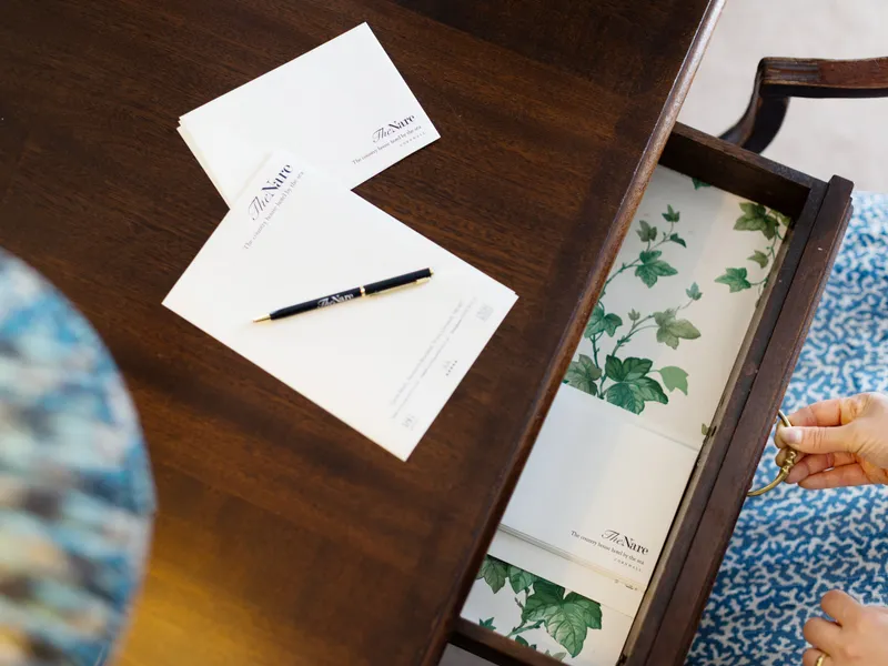 Writing desk with The Nare stationery, a pen and an open drawer lined with floral paper
