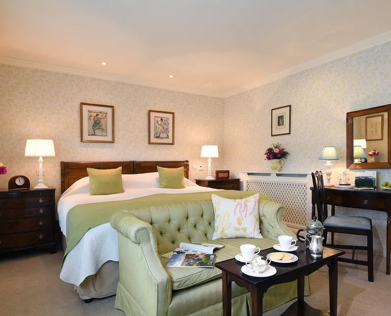 Elegant guest bedroom with a double bed, green upholstered sofa, dressing table and tea set in a cosy seating area