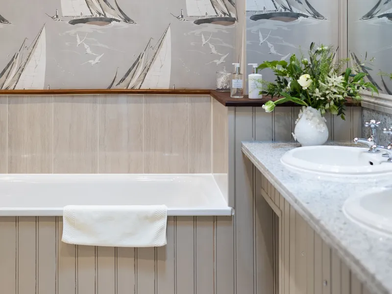Elegant bathroom with sailing boat wallpaper, bath, double sink vanity and fresh flowers